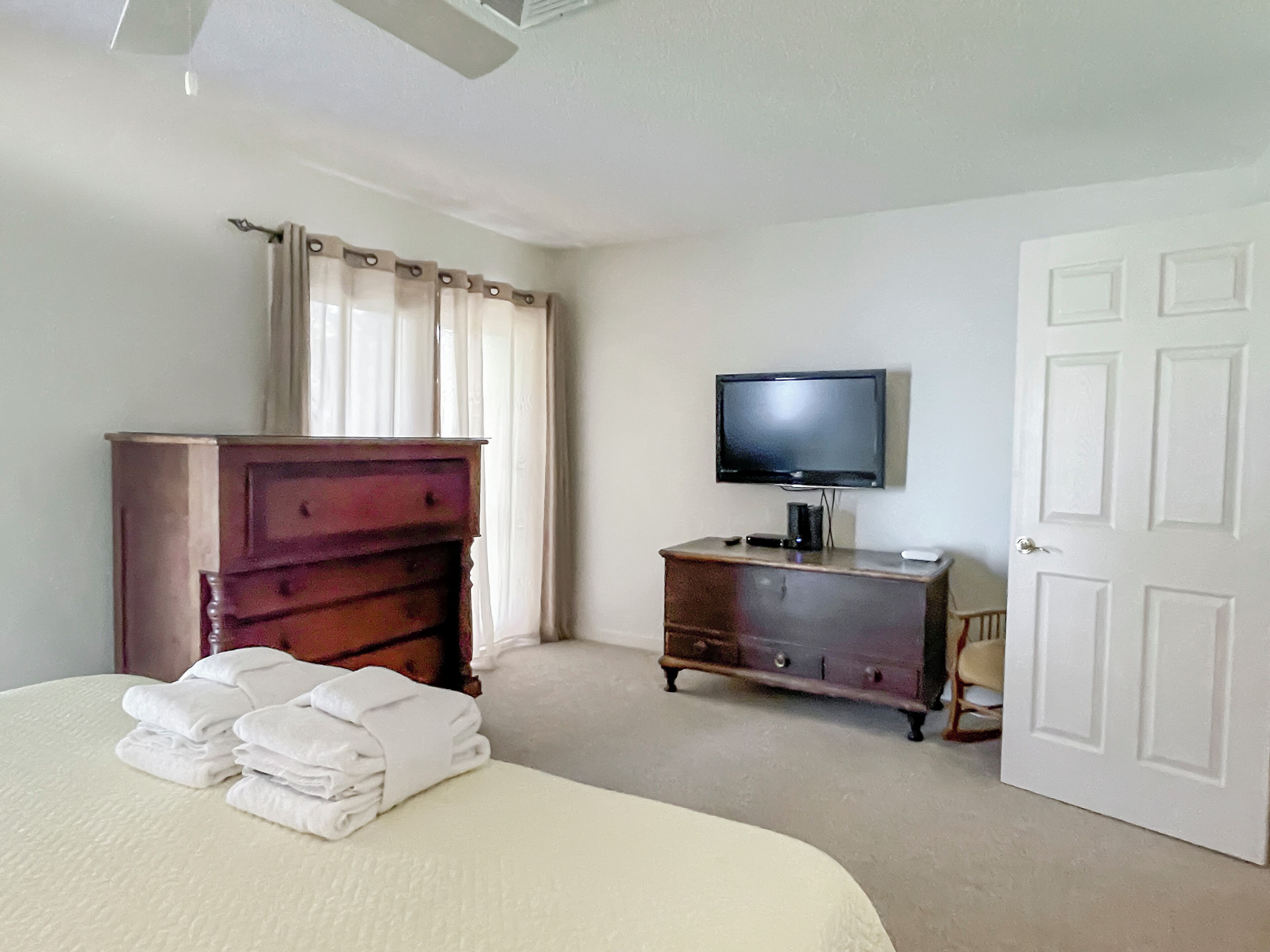 Un dormitorio con cama, cómoda, televisor y una puerta.