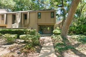 A two-story building with a front porch, a pathway leading to the entrance, and a well-maintained garden with various shrubs and a large tree. - 505 Plantation Club Villas at The Sea Pines Resort (Hilton Head Island)