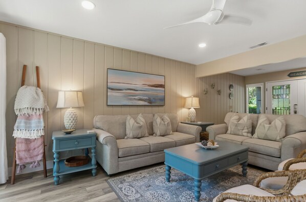 A living room with a beige sofa, a blue coffee table, and a painting on the wall. - 505 Plantation Club Villas at The Sea Pines Resort (Hilton Head Island)