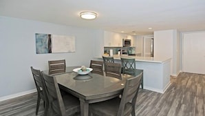 A dining area with a round table and six chairs, a kitchen in the background, and a wooden floor. - 524 Plantation Club Villas at The Sea Pines Resort (Hilton Head Island)