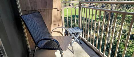 Un balcón con una silla de metal y una mesita pequeña, con vista a un césped verde y árboles.