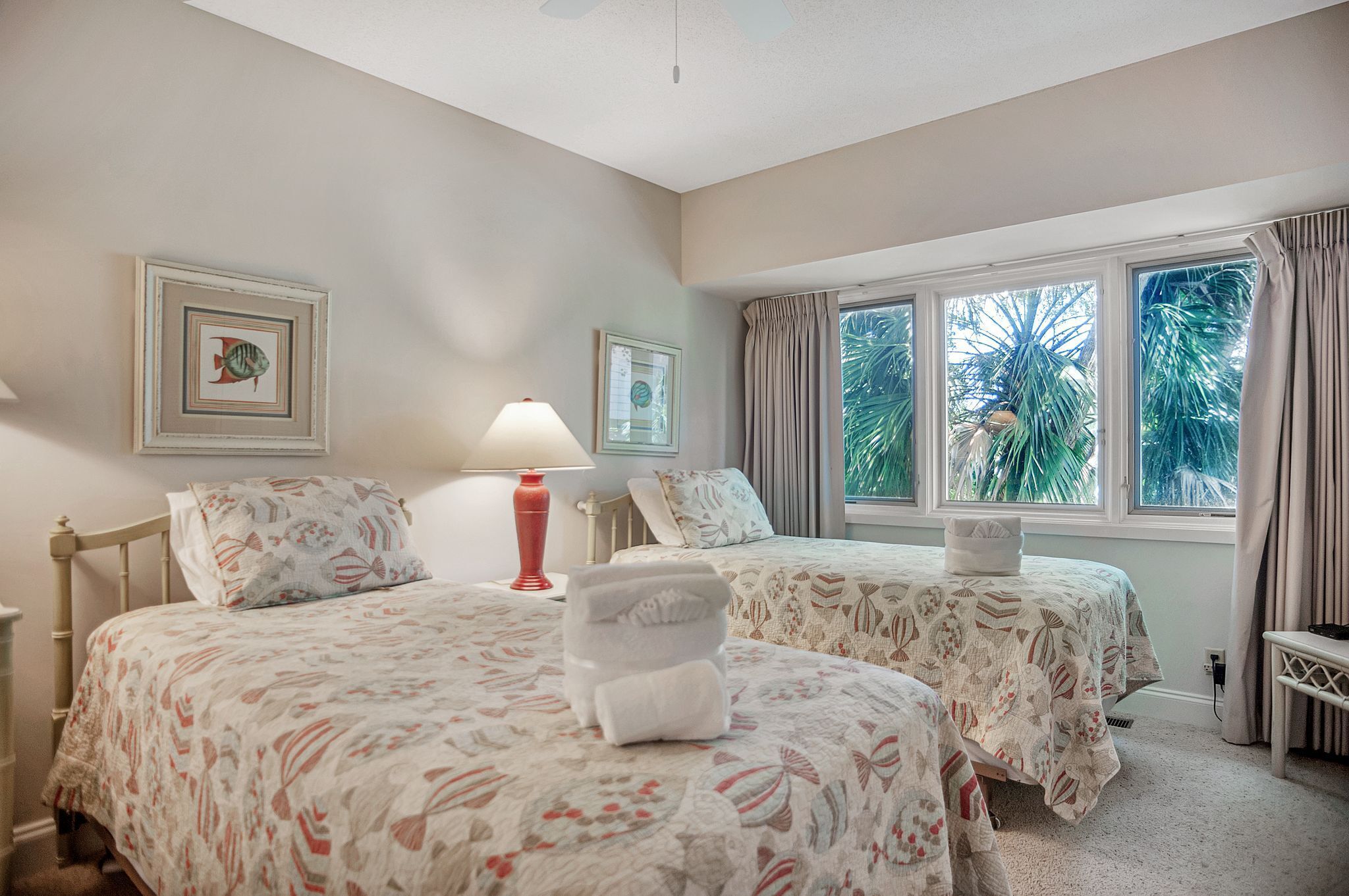 A bedroom with two beds, a nightstand, a lamp, and a window with curtains.
