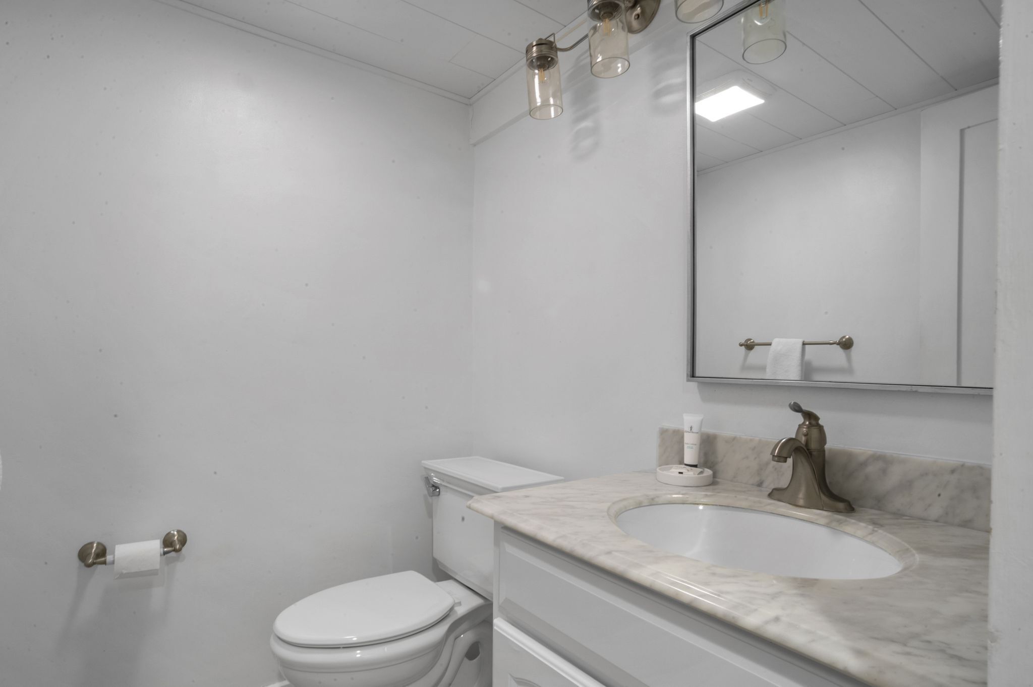 Un baño con inodoro blanco, un lavamanos con encimera de mármol y un espejo sobre el lavamanos.