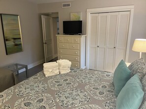 Een slaapkamer met een bed, een dressoir, een televisie, een kast en een schilderij aan de muur.