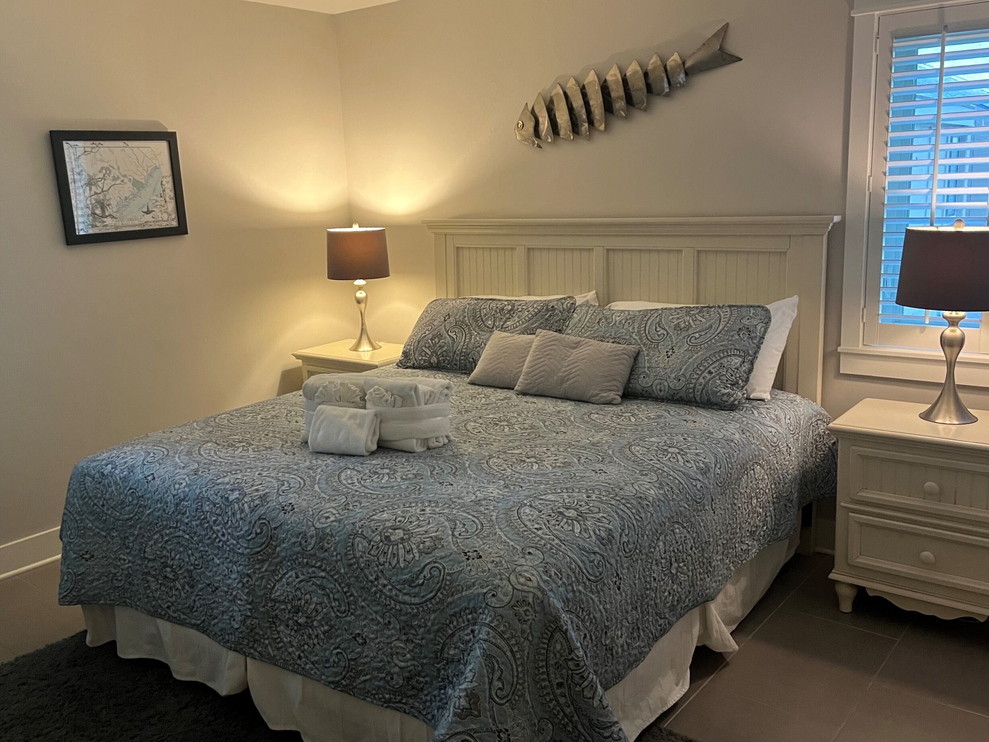 A neatly made bed with a patterned bedspread, a fish-shaped wall decoration, and a framed picture on the wall.