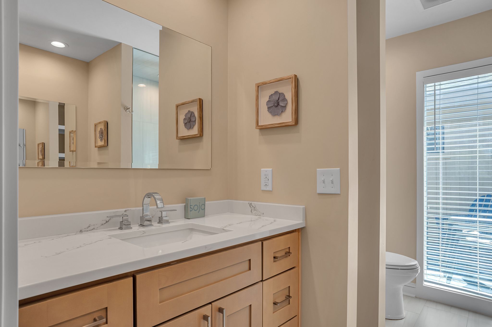 A bathroom with a large mirror, two sinks, wooden cabinets, and framed artwork on the wall.