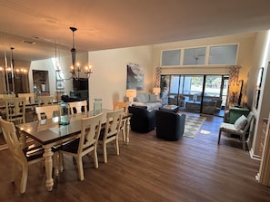 A spacious living area with a dining table, chairs, a sofa, and a large window with a view. - 552 Ocean Course at The Sea Pines Resort (Hilton Head Island)