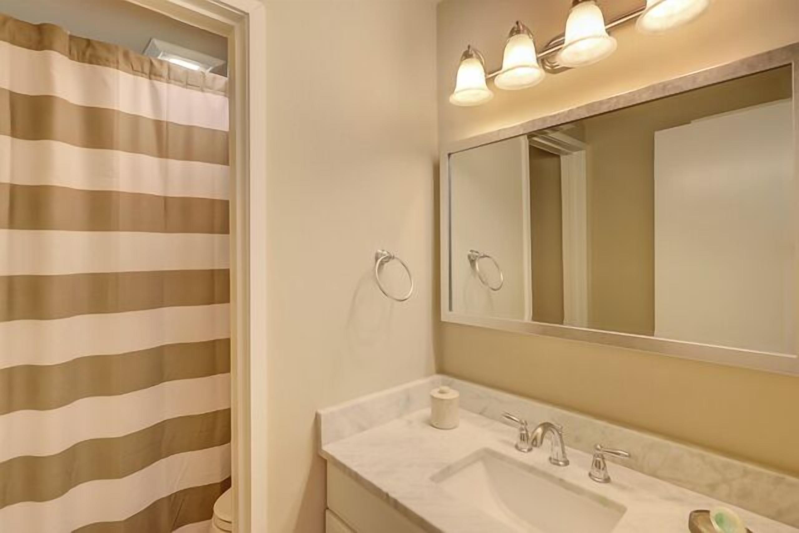 Une salle de bain avec un rideau de douche à rayures, un lavabo avec un miroir au-dessus et un porte-serviettes fixé au mur.
