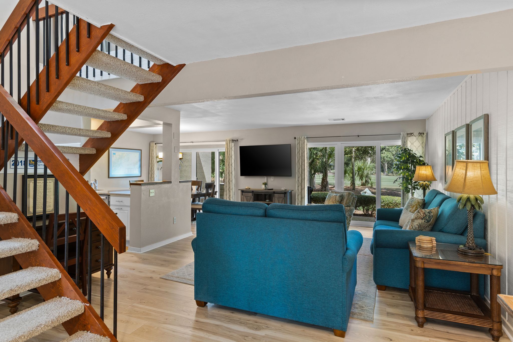 Amplia sala de estar con una escalera de madera, un sofá azul grande y un televisor al fondo.