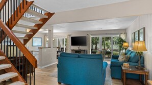 A spacious living area with a wooden staircase, a large blue sofa, and a television in the background. - 485 Plantation Club Villas at The Sea Pines Resort (Hilton Head Island)