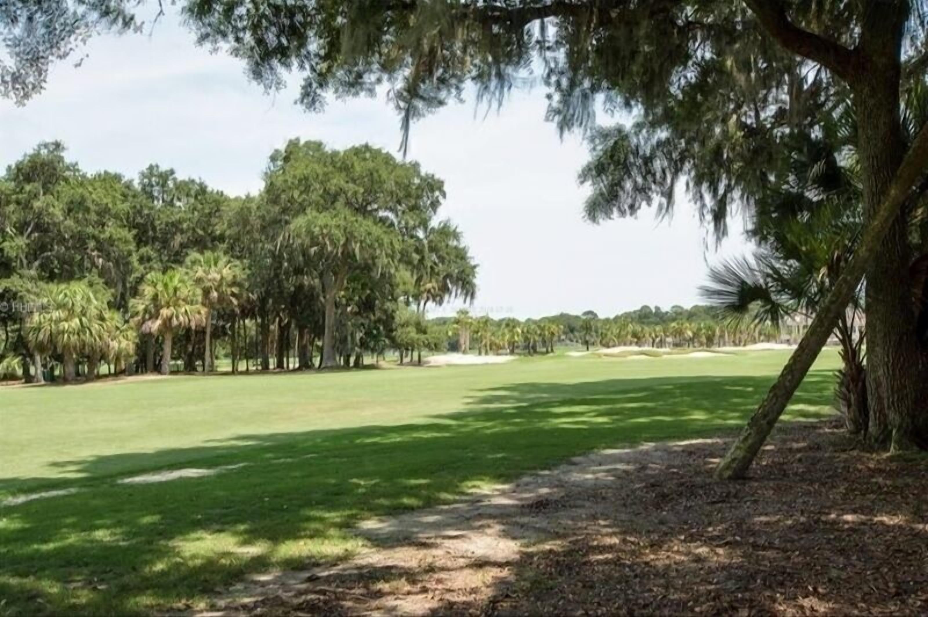 A golf course with a clear path, surrounded by trees and a clear sky.