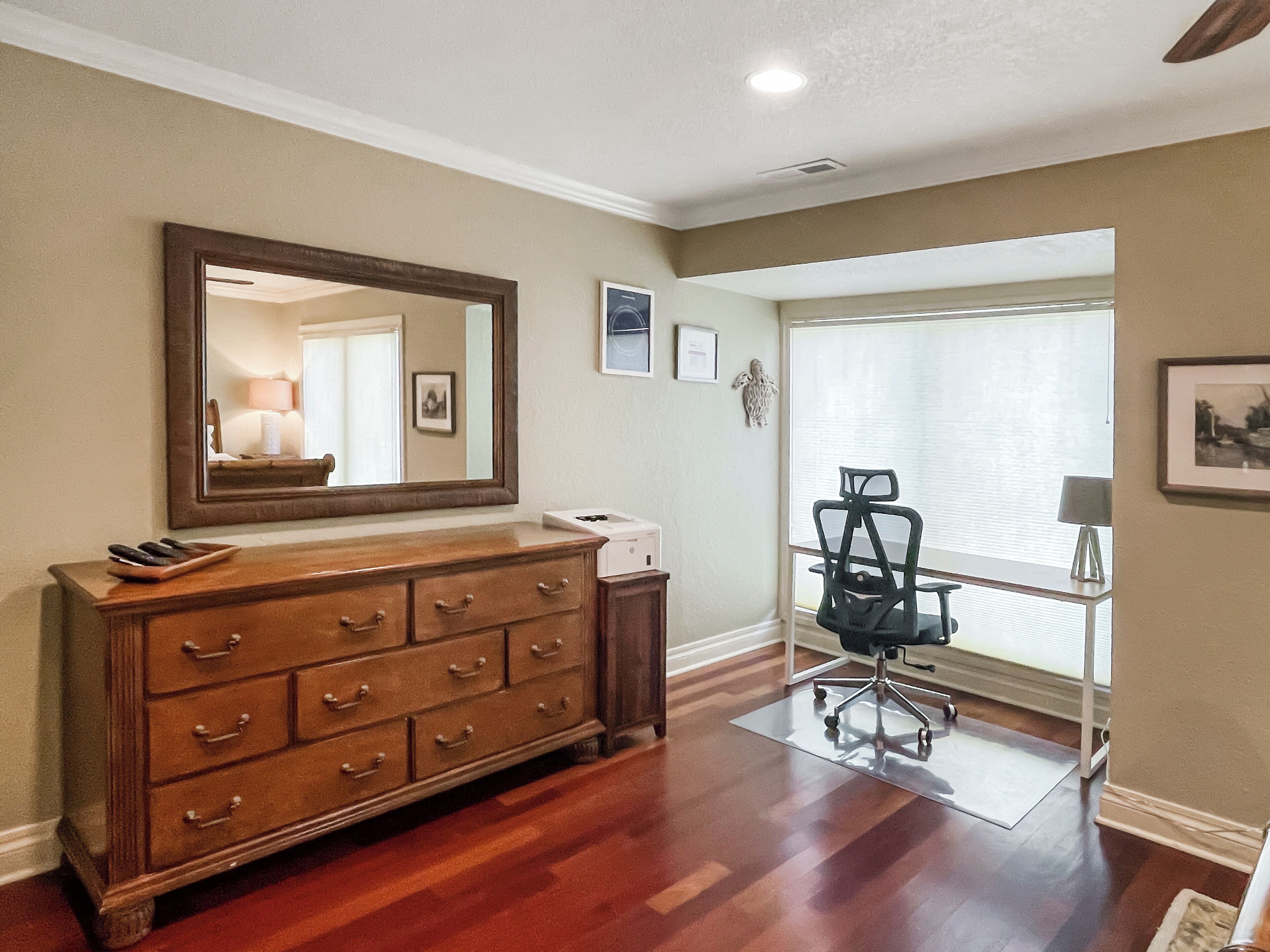 Una habitación con un aparador de madera, un espejo, un escritorio con una silla y una ventana con persianas.