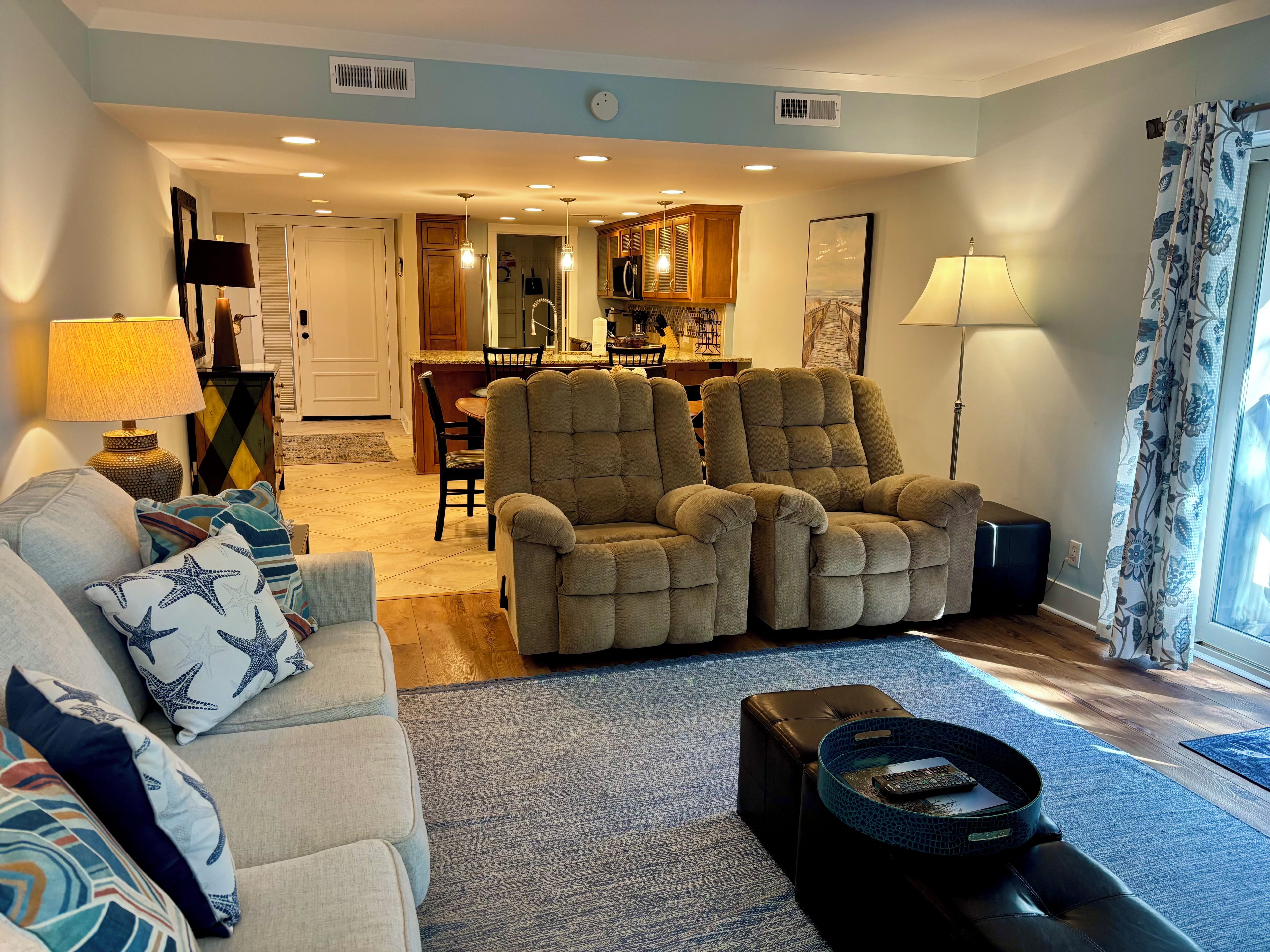 A living room with a sofa, armchairs, a coffee table, and a dining area in the background.