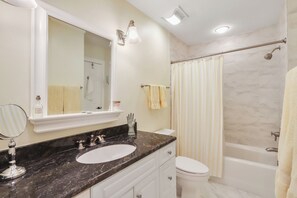 Une salle de bain avec un lavabo en marbre, des toilettes, une baignoire et un rideau de douche.