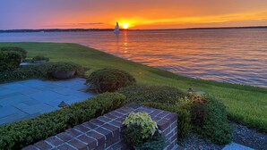 A sunset view over a calm body of water with a grassy area and a brick pathway leading to a dock.
