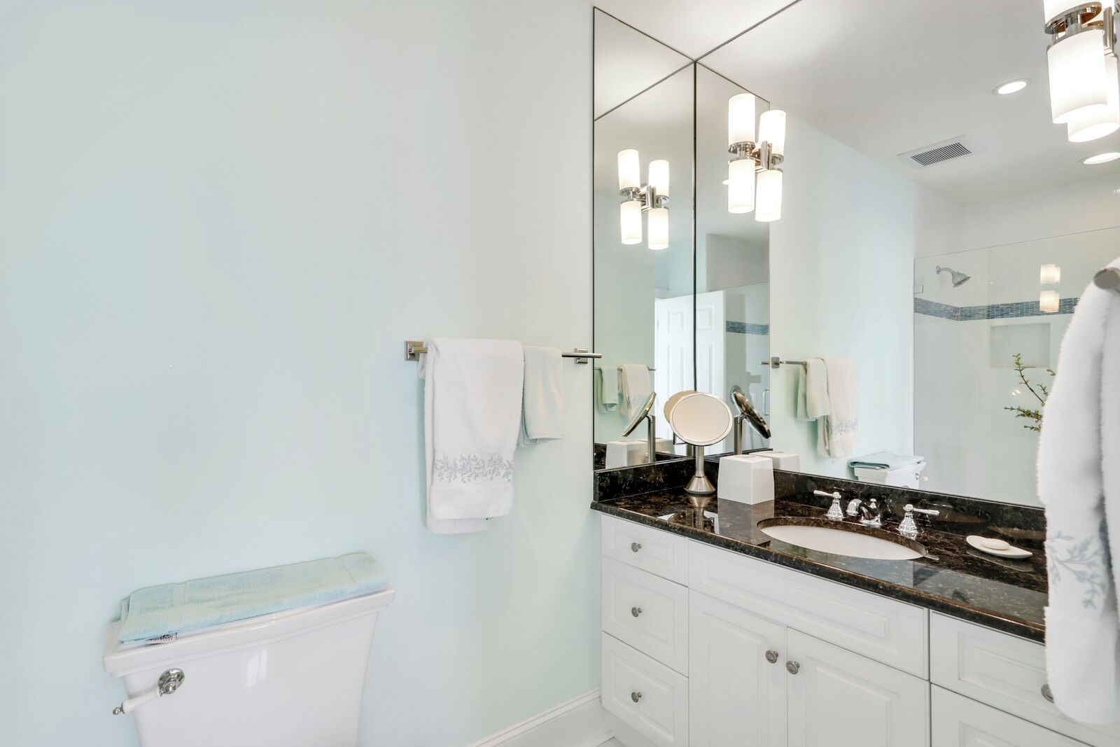 A modern bathroom with a large mirror, white cabinets, and a marble countertop.