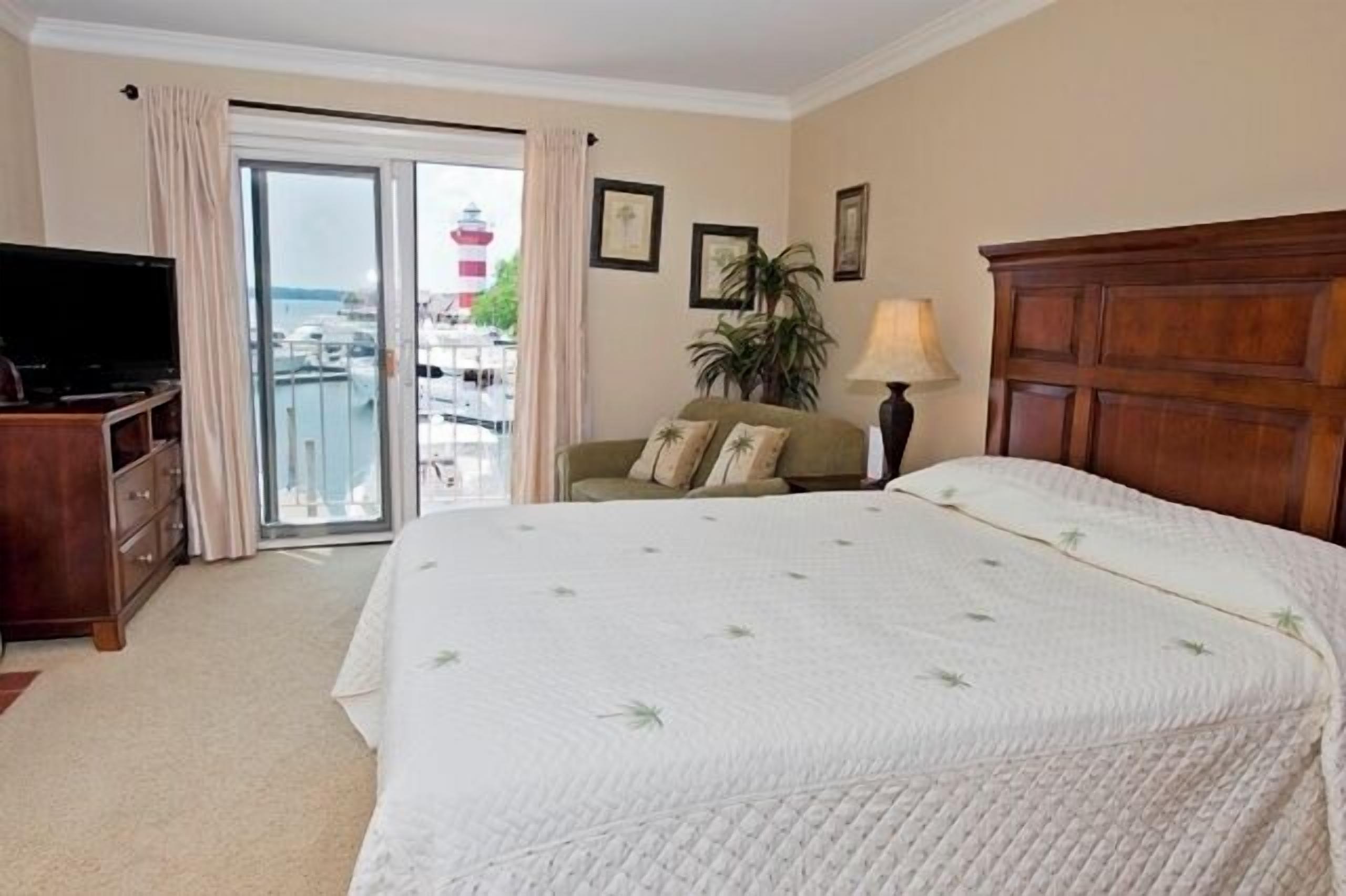 Une chambre d’hôtel avec un grand lit, une télévision, un balcon donnant sur un phare et une tête de lit en bois.