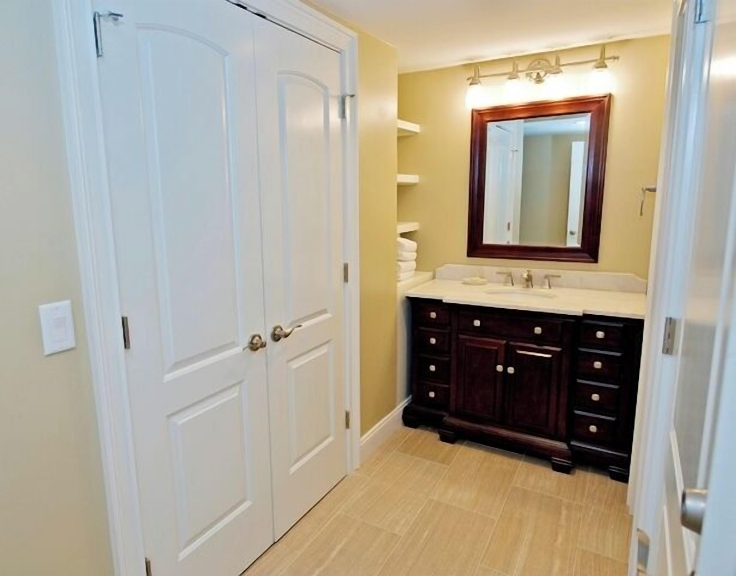 A bathroom with a white door, a vanity with dark wood cabinets, and a mirror above the sink.