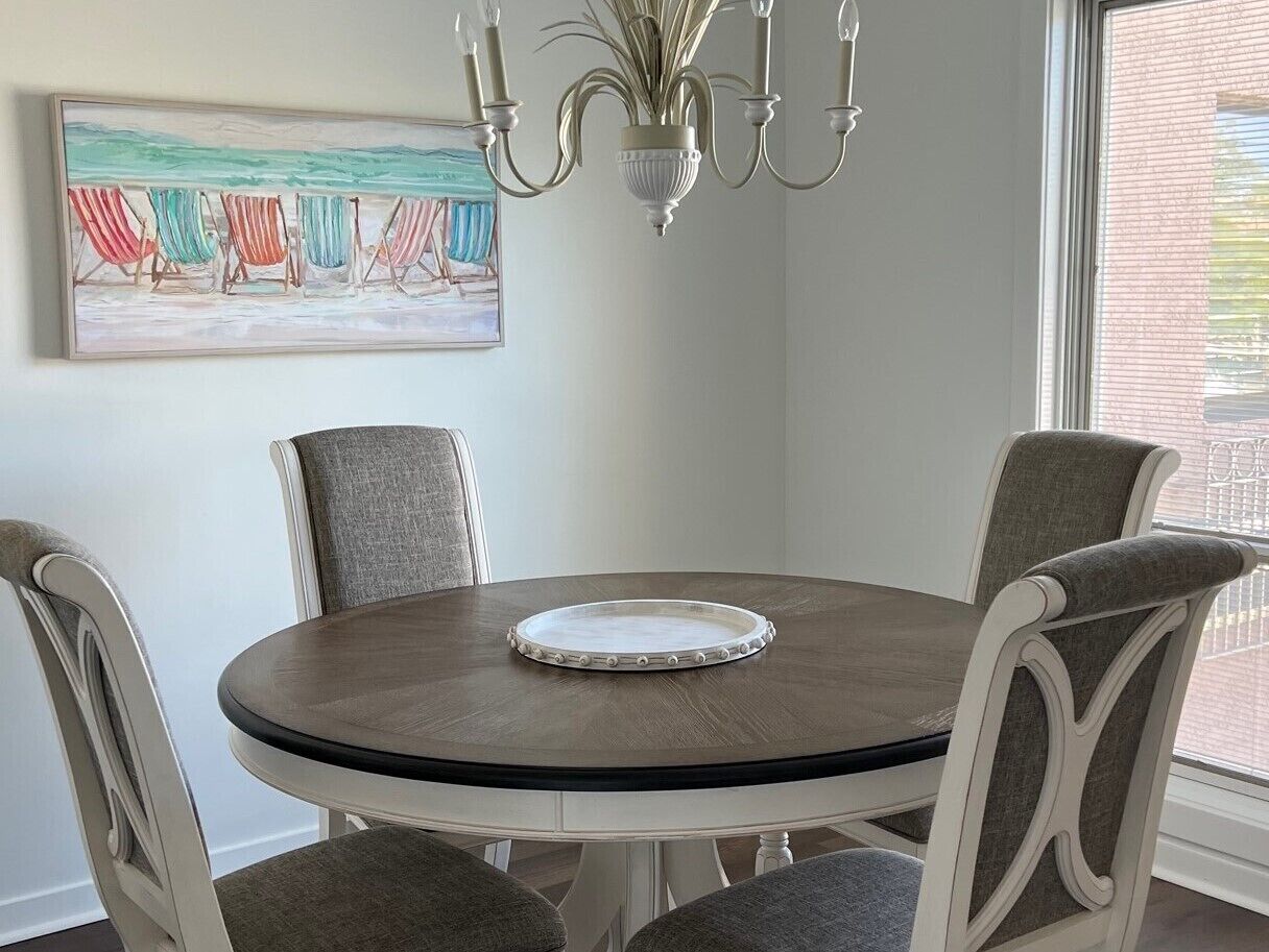 A dining table with four chairs, a chandelier, and a beach-themed painting on the wall.