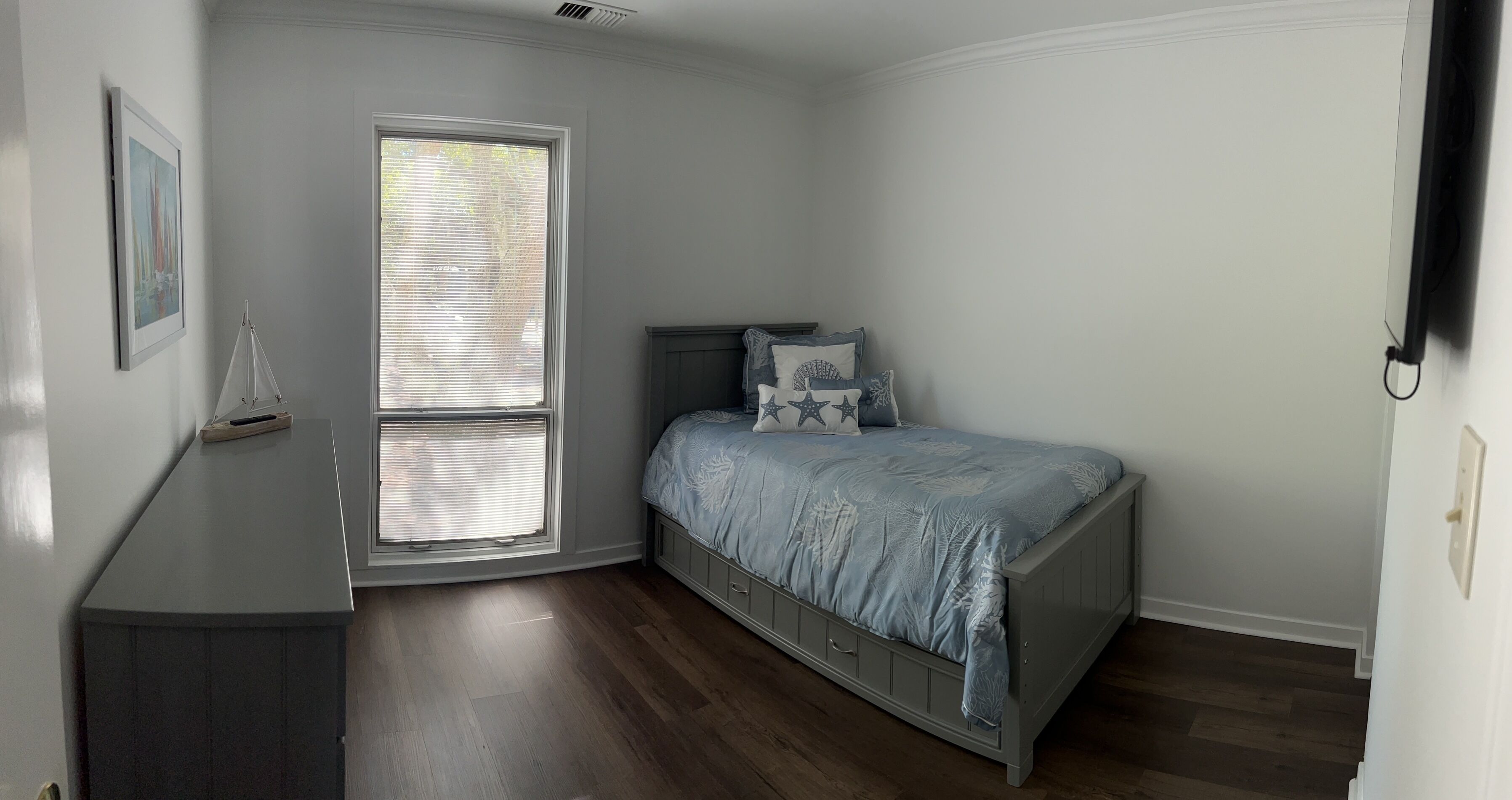 A bedroom with a bed, a window with blinds, a bedside table, and a framed picture on the wall.