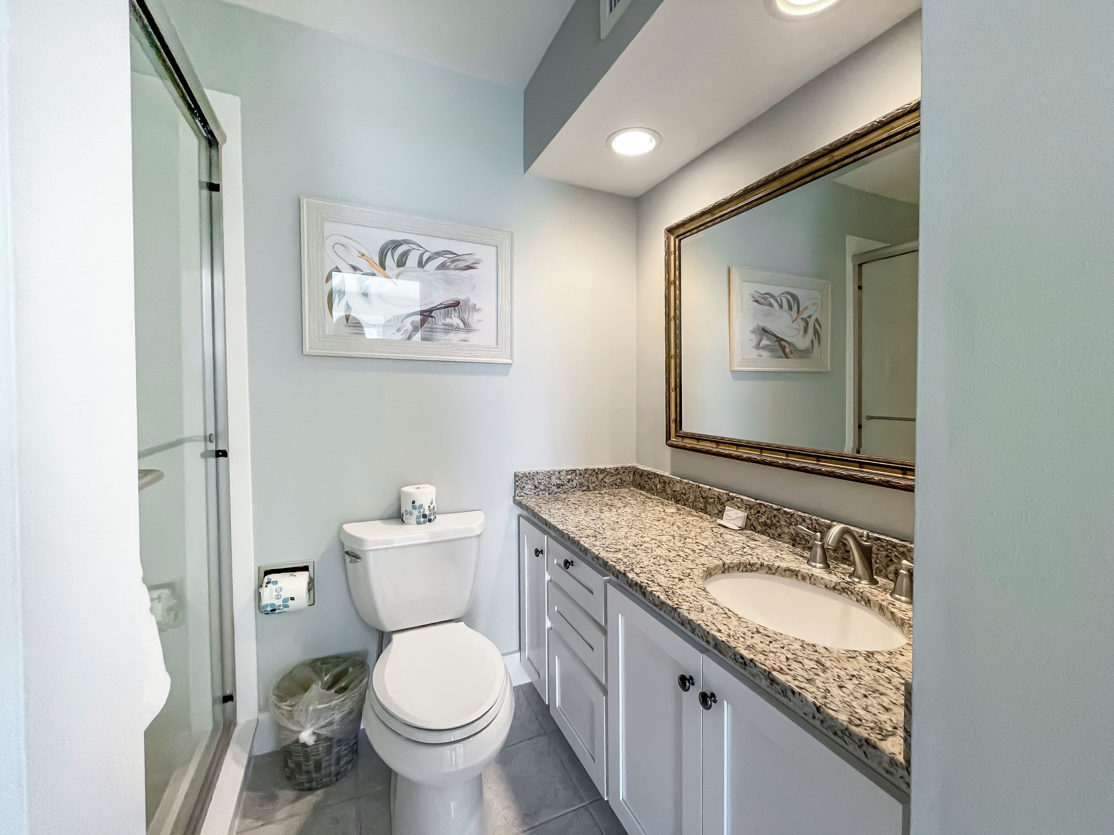 A modern bathroom with a toilet, sink, and shower. There are framed artworks on the wall and a large mirror above the sink.