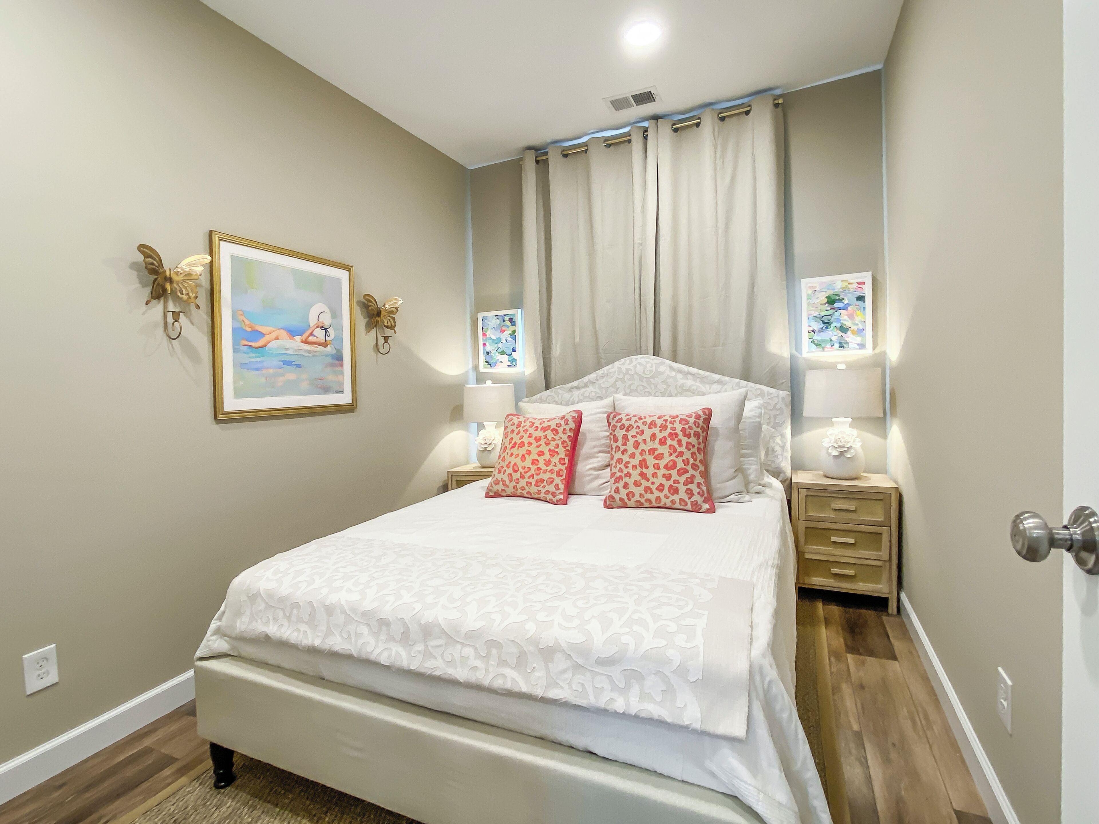 Un dormitorio con cama, mesitas de noche, un cuadro y una ventana con cortinas.
