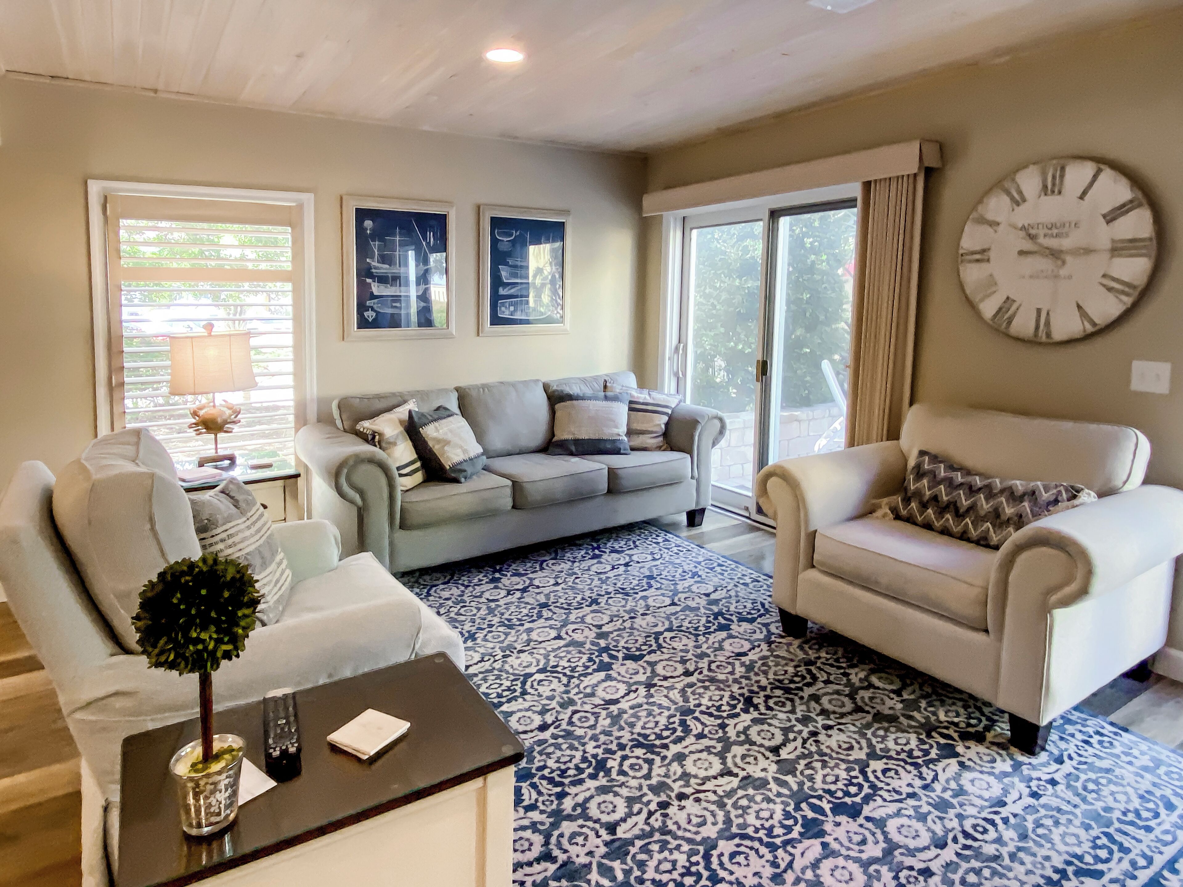 A living room with a grey sofa, a white armchair, a patterned rug, and a large wall clock.