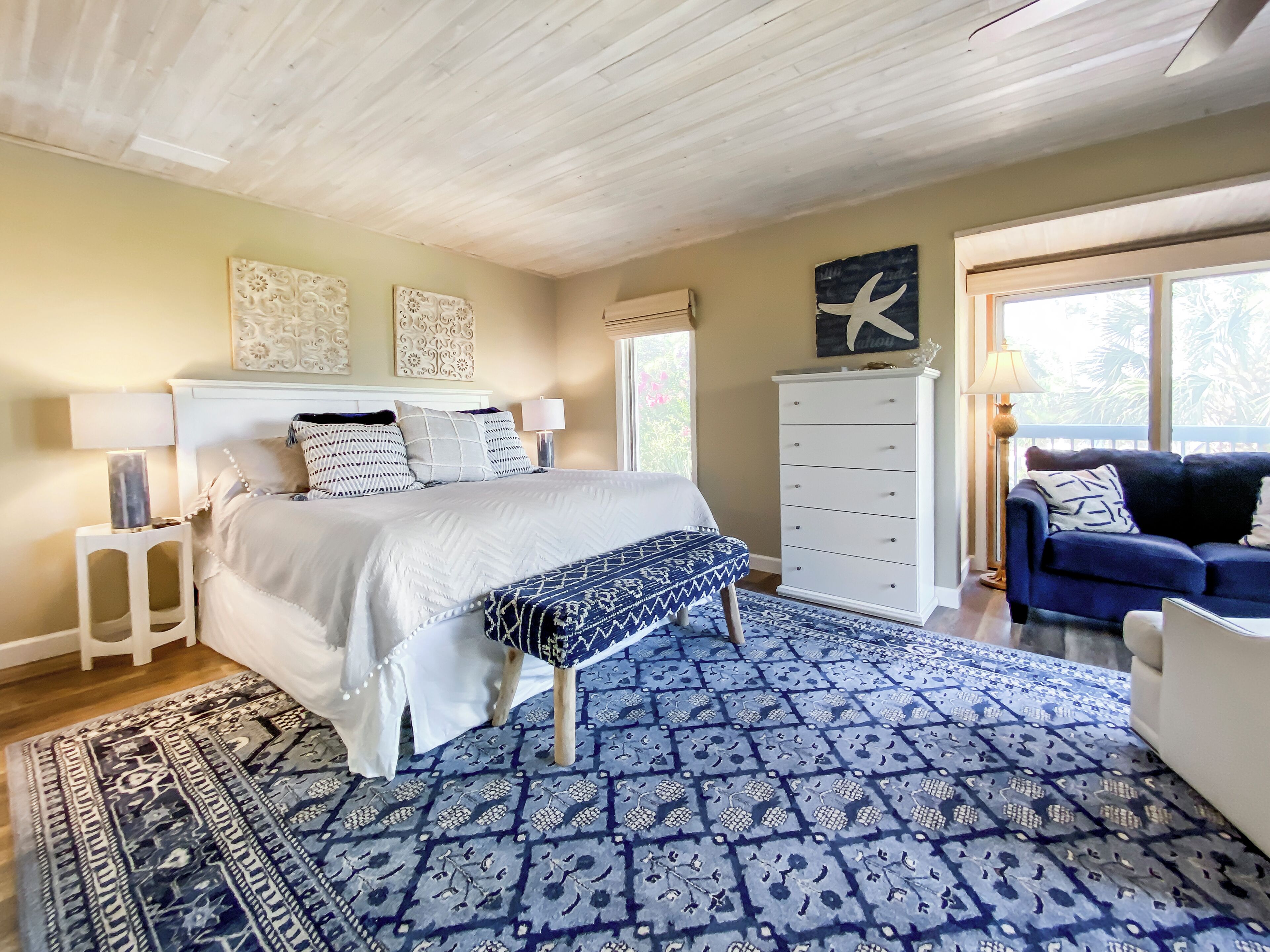 Um quarto com uma cama, mesas de cabeceira, cômoda, um sofá azul e um tapete estampado.