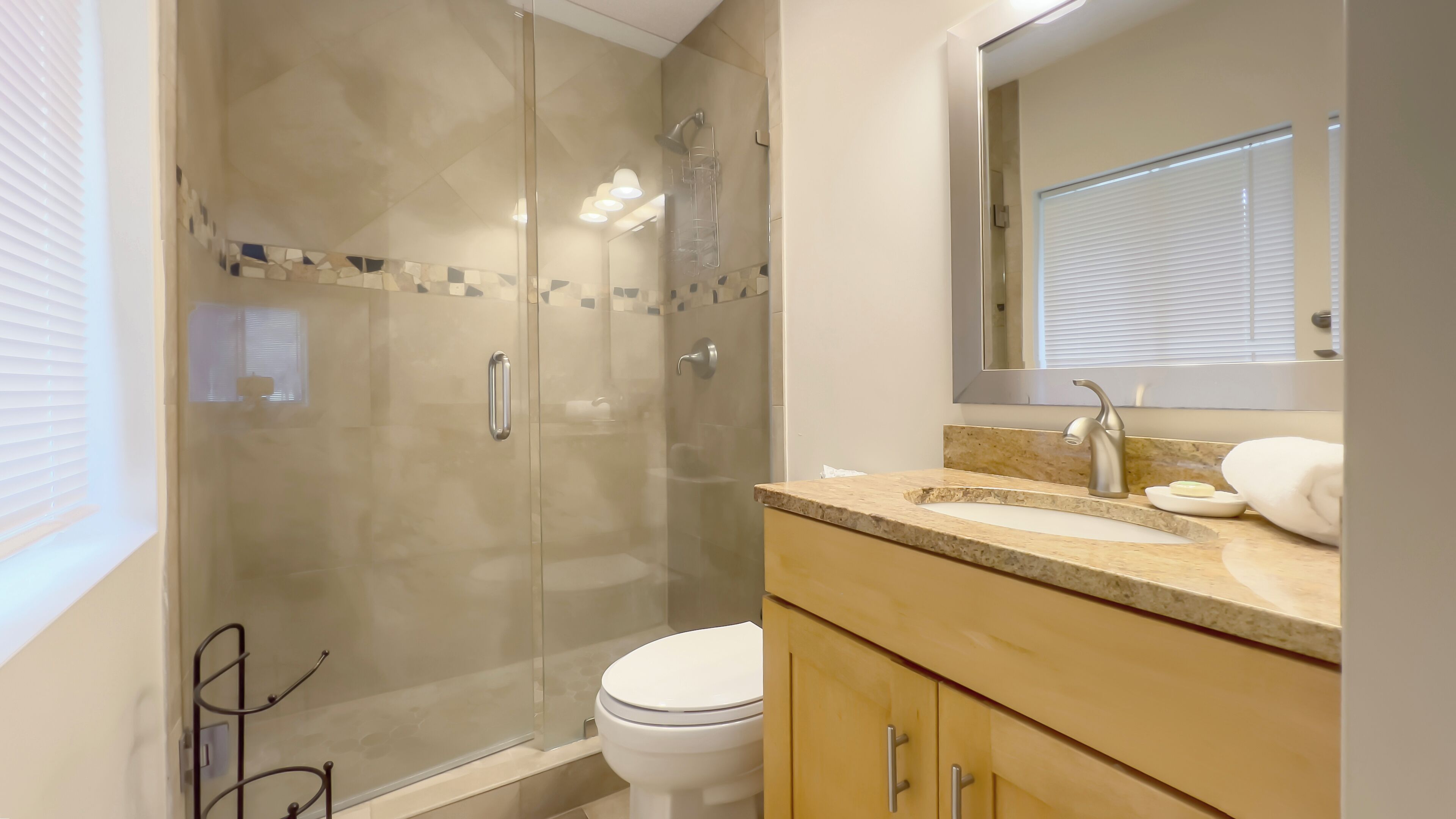 A modern bathroom with a glass-enclosed shower, a toilet, and a vanity with a sink and mirror.
