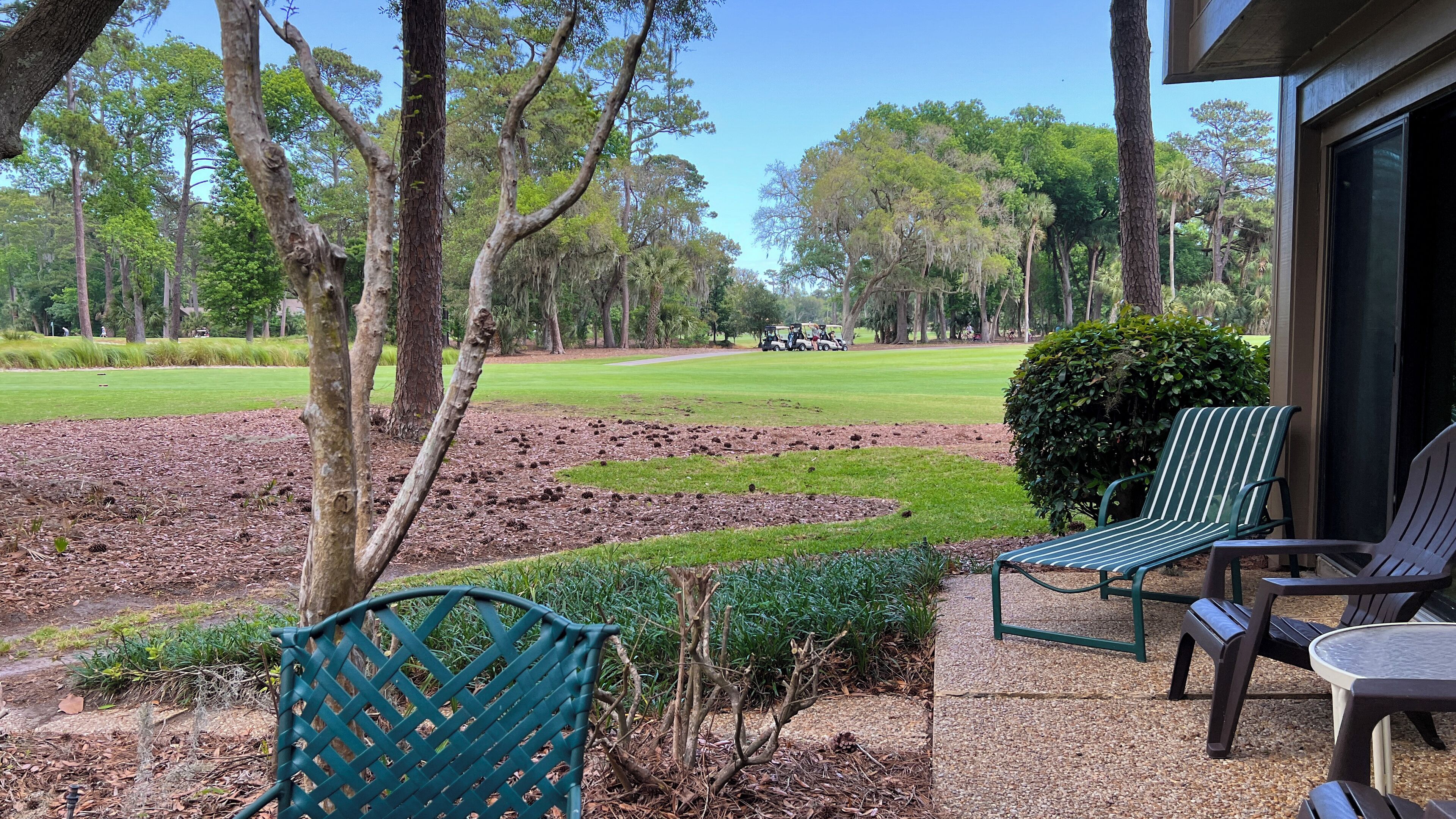 A patio with outdoor seating, a golf course in the background, and a building with a large window.