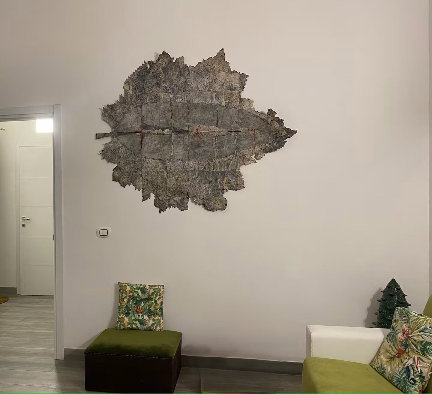 Et værelse med et stort vægmaleri, en grøn polstret bænk og en hvid sofa med en blomstret pude.