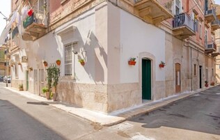 Un edificio con fachada blanca, puerta verde y plantas en macetas en la planta baja.