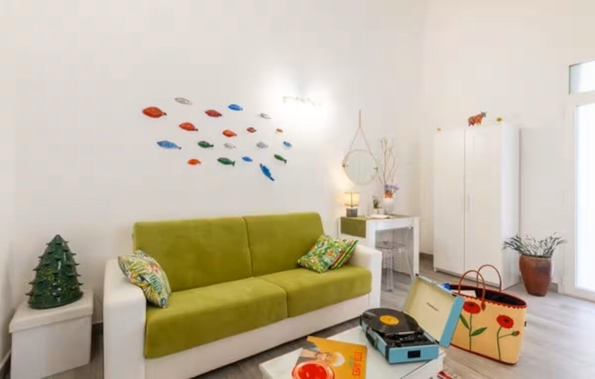 A living room with a green sofa, a small Christmas tree, a wall with colorful fish decals, a lamp, a white cabinet, and a potted plant.