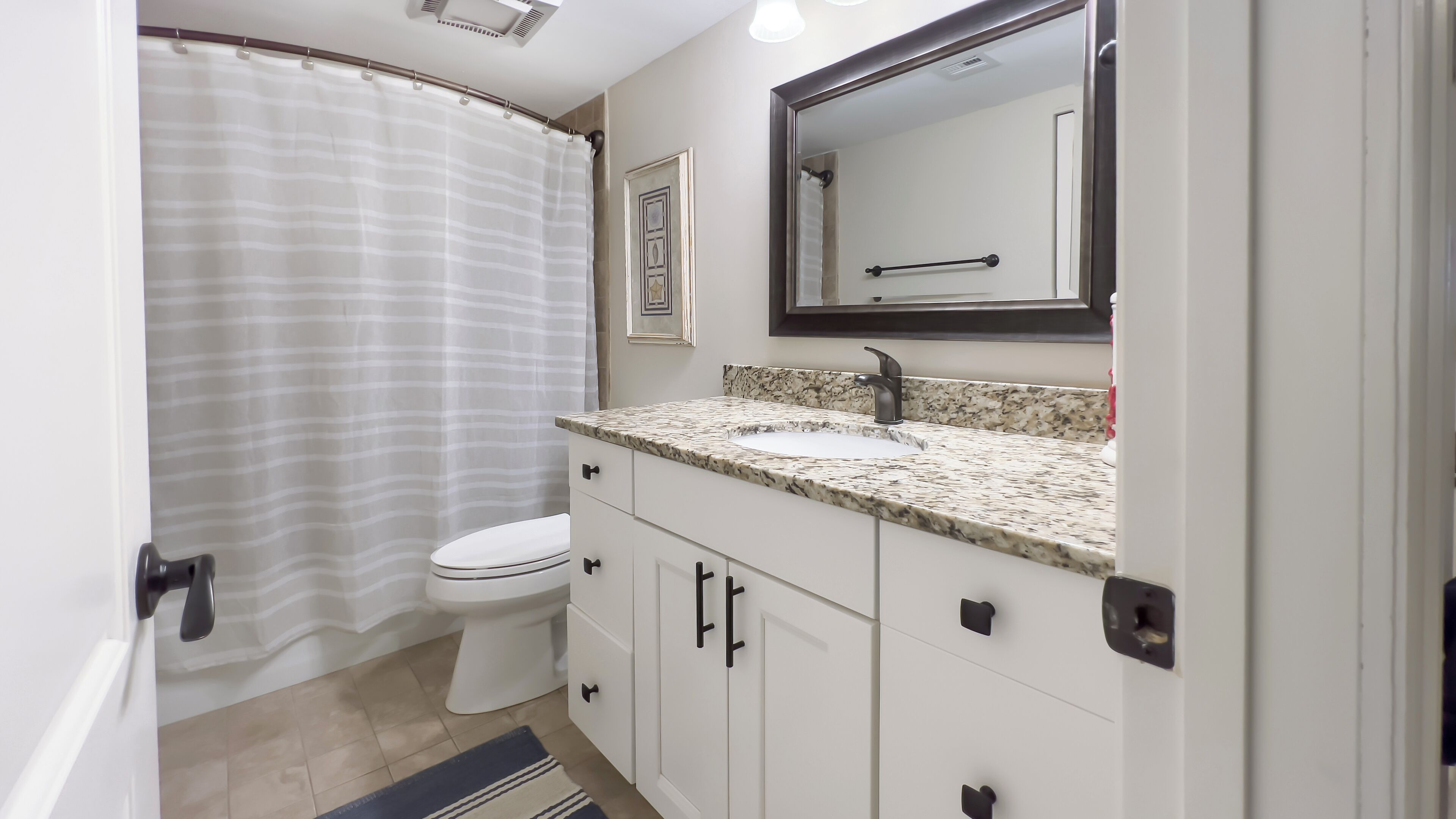 A bathroom with a white toilet, a granite countertop sink, and a large mirror above it.