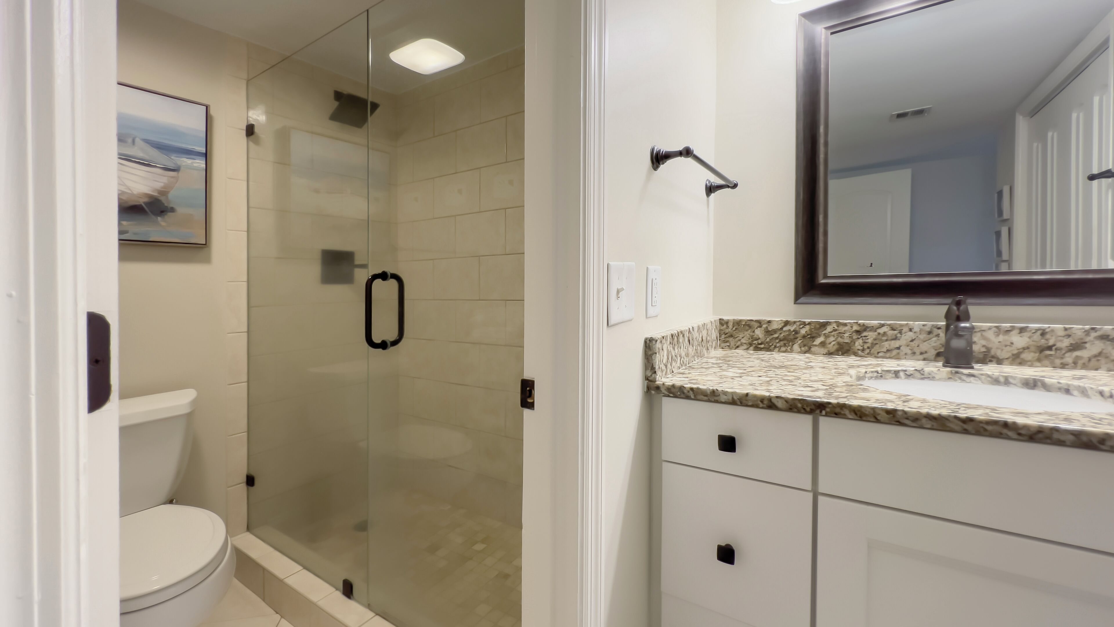 A modern bathroom with a glass-enclosed shower, a white toilet, and a marble countertop with a sink and mirror.