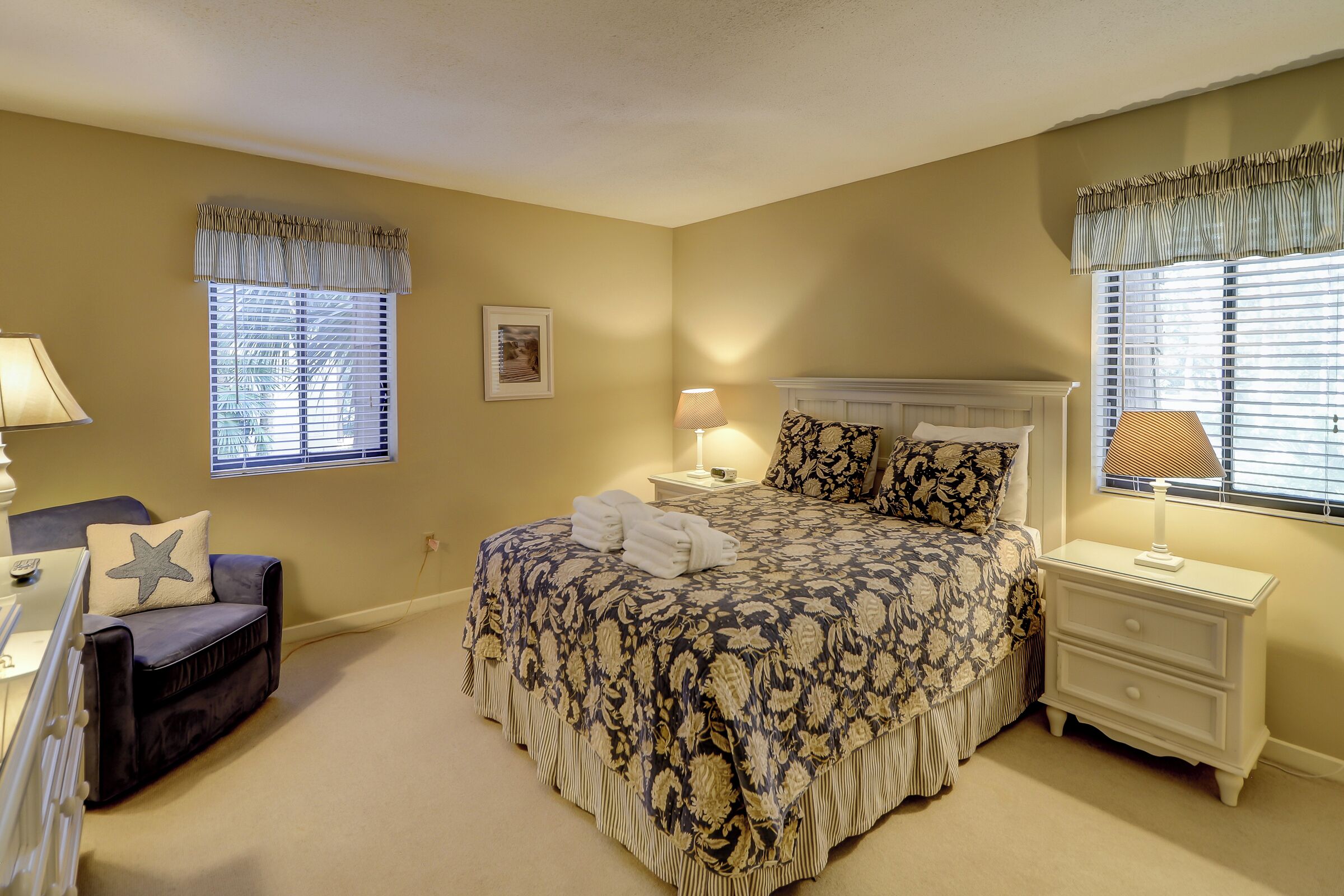 A bedroom with a large bed, bedside tables with lamps, a chair, and a window with blinds.
