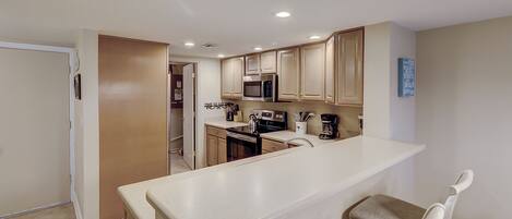 A modern kitchen with a central island, stainless steel appliances, and light-colored cabinetry.