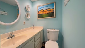 A bathroom with a beige sink, a white toilet, and a framed painting of a building. - 744 Schooner Court at The Sea Pines Resort (Hilton Head Island)