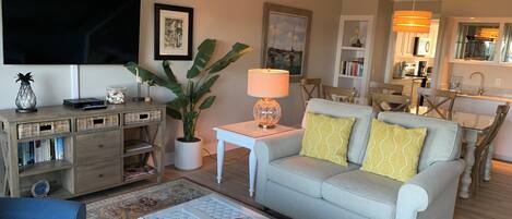 A living room with a sofa, coffee table, TV, and a dining area with chairs and a table.