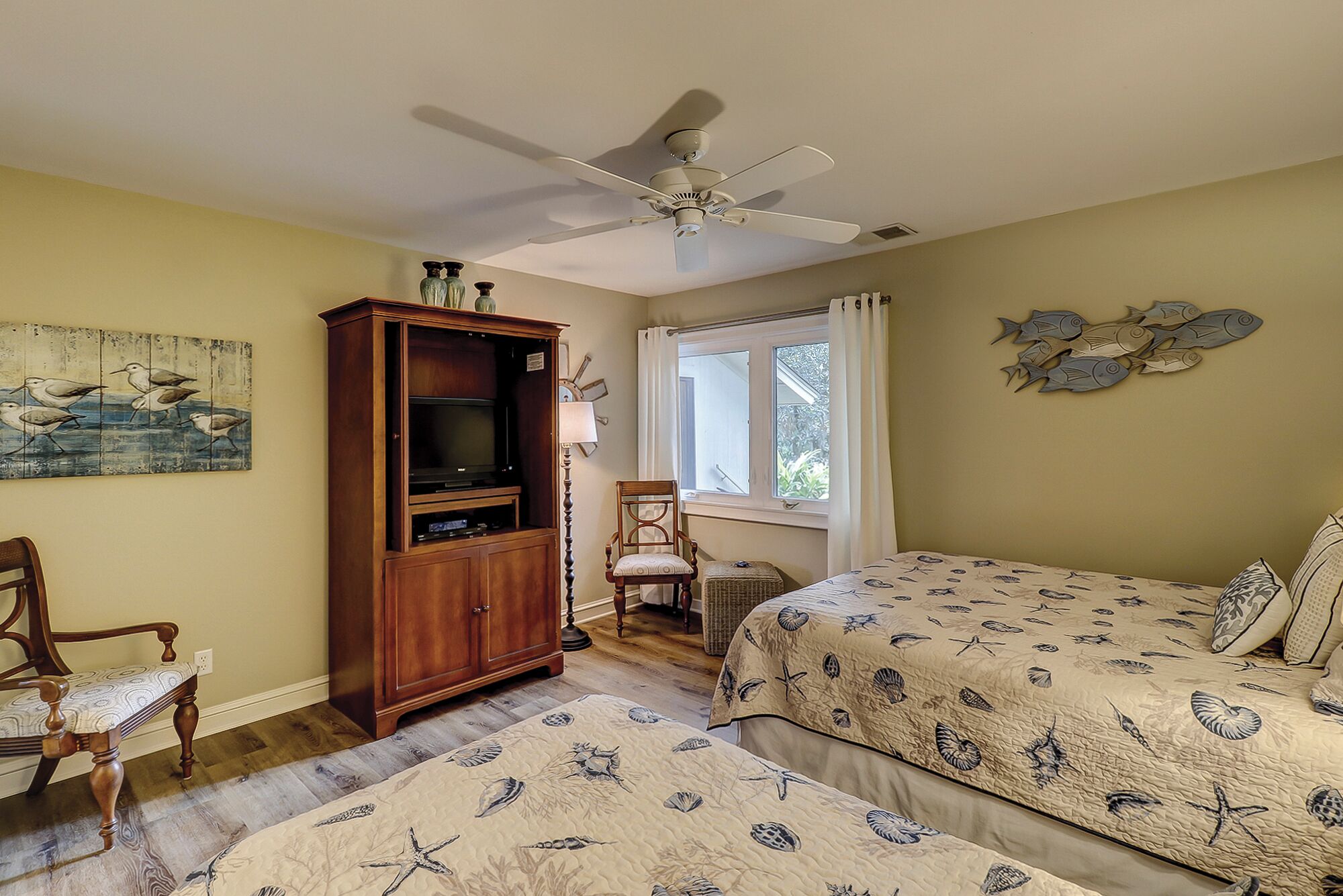 A bedroom with a bed, a wooden cabinet, a chair, a ceiling fan, and a window with curtains.