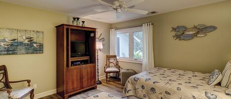 A bedroom with a bed, a wooden cabinet, a chair, a ceiling fan, and a window with curtains.