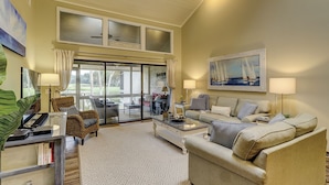 A spacious living room with a large sliding glass door leading to a patio, a comfortable sofa set, a coffee table, and a painting of sailboats. - 561 Ocean Course at The Sea Pines Resort (Hilton Head Island)