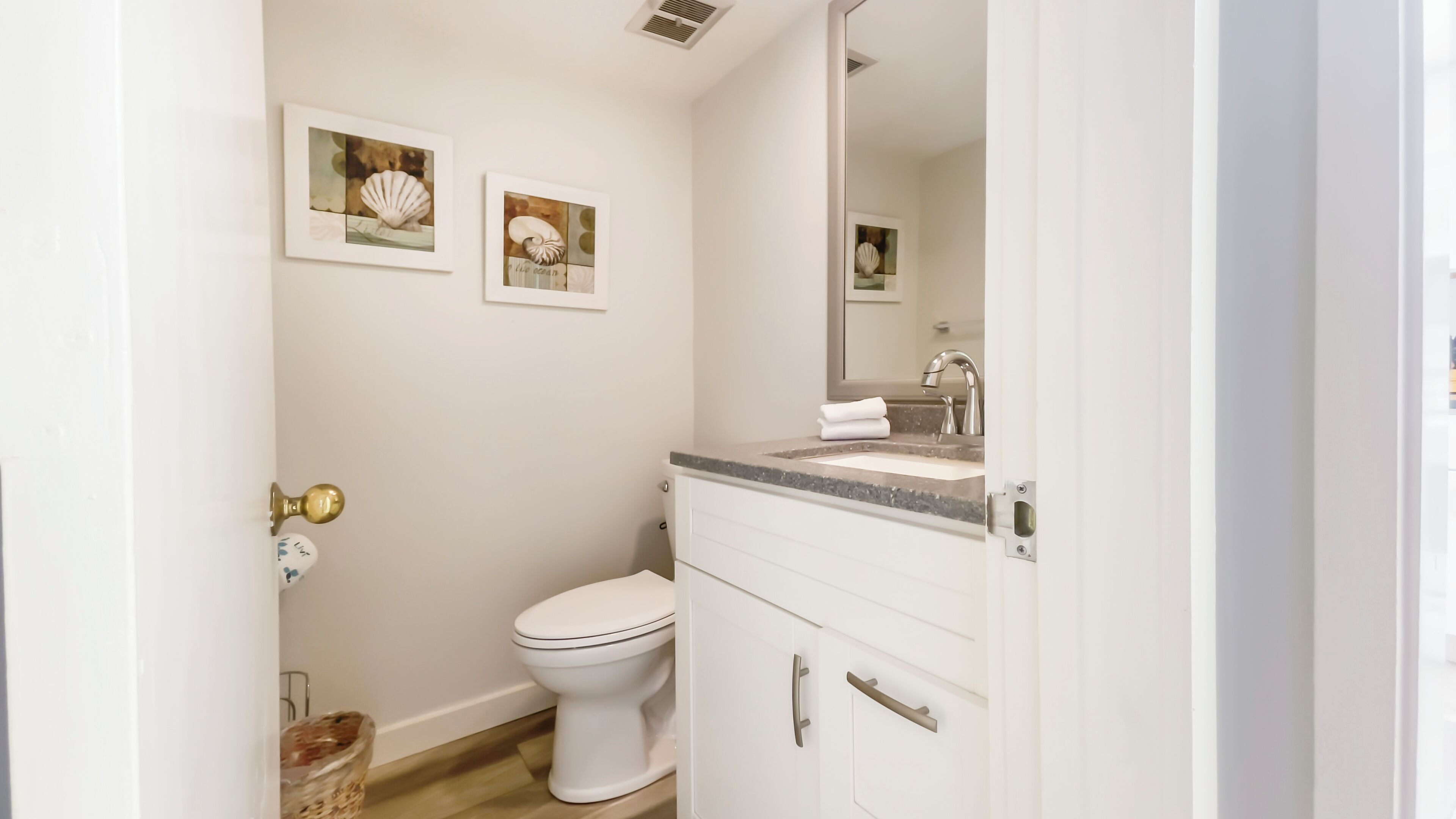 A bathroom with a toilet, a sink with a mirror, and two framed pictures on the wall.