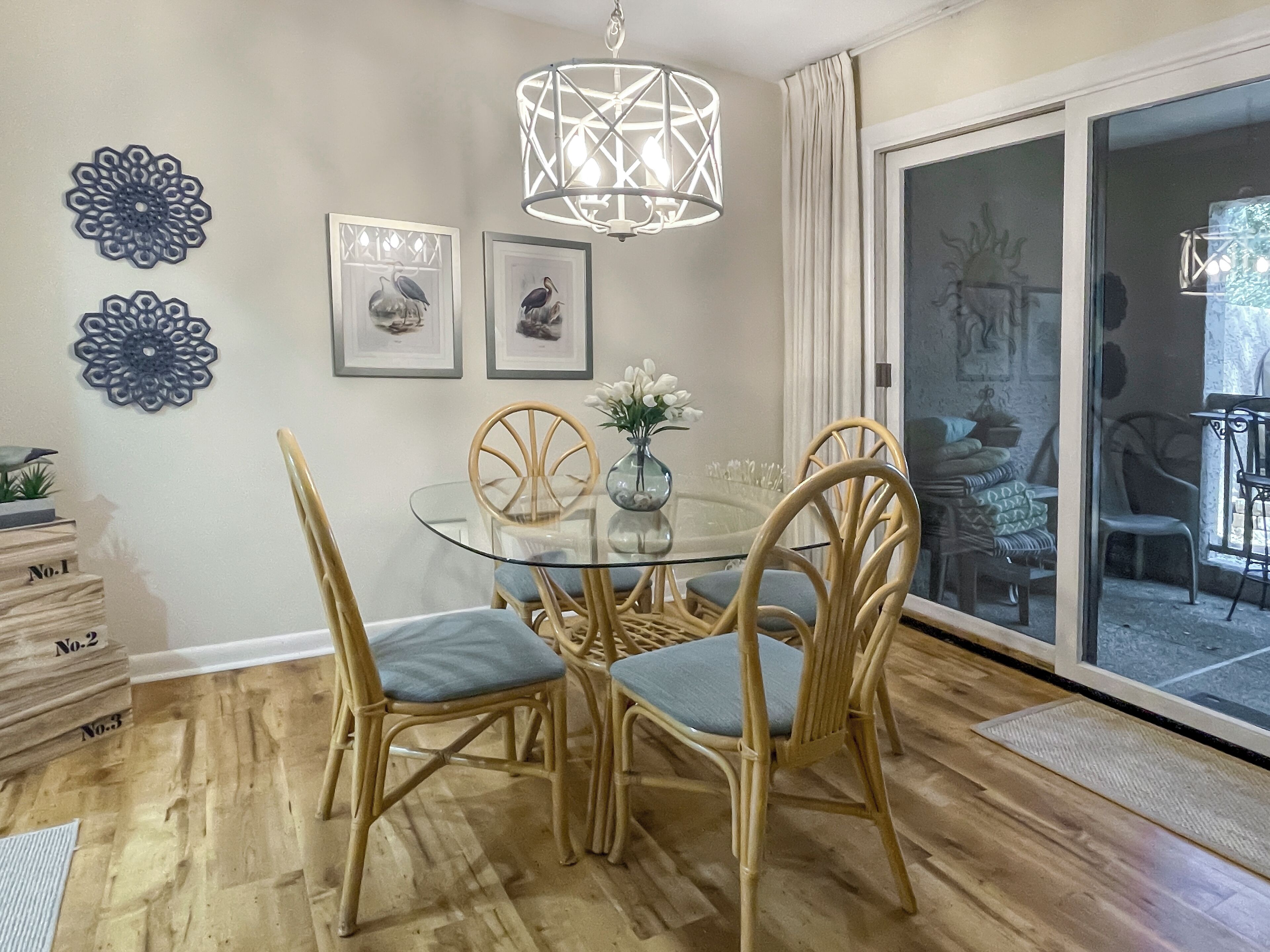 Un comedor con una mesa de vidrio rodeada de sillas de mimbre, un accesorio de iluminación decorativo y obras de arte en la pared.
