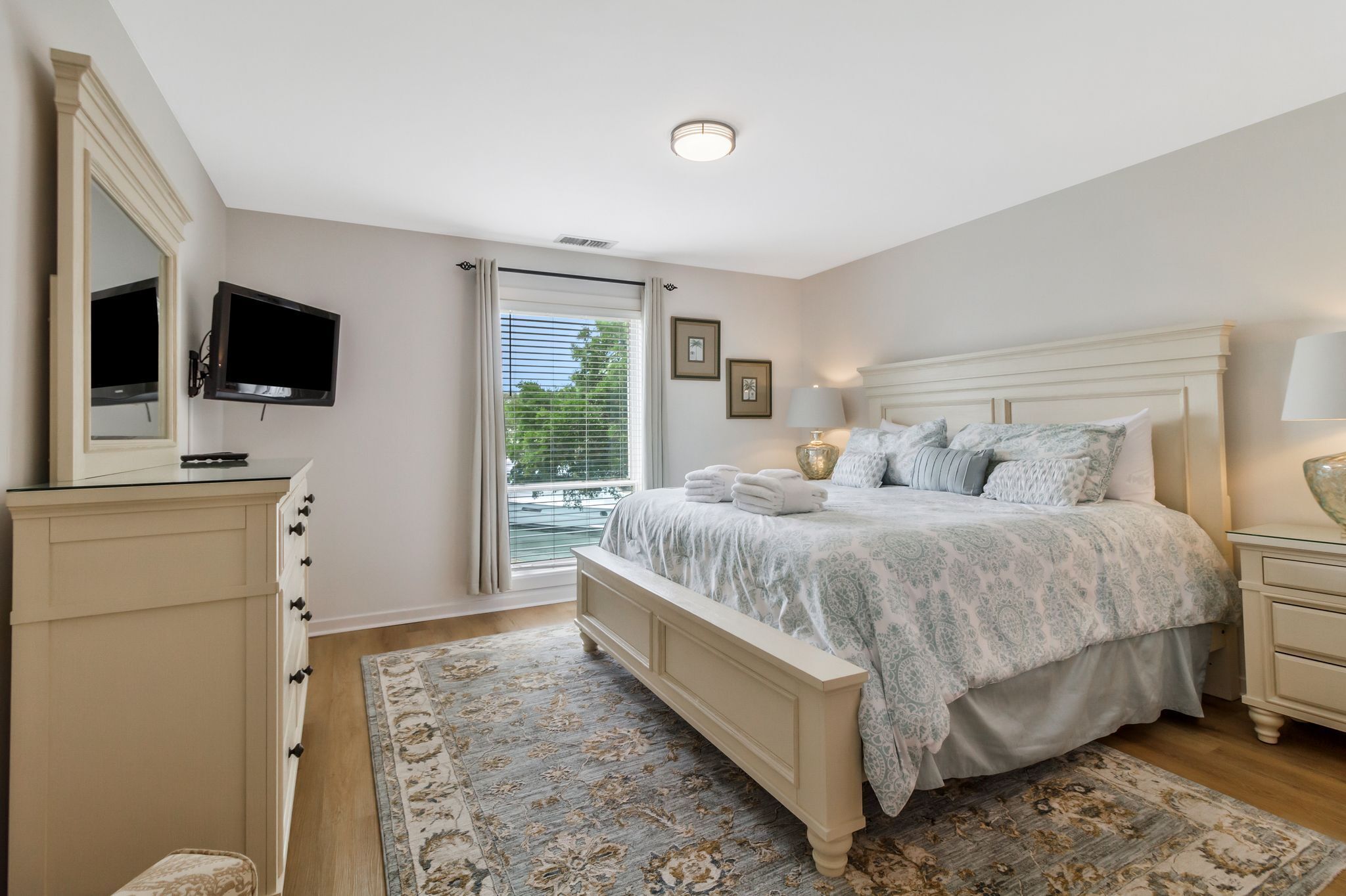 A bedroom with a bed, bedside tables, a TV, and a window with curtains.