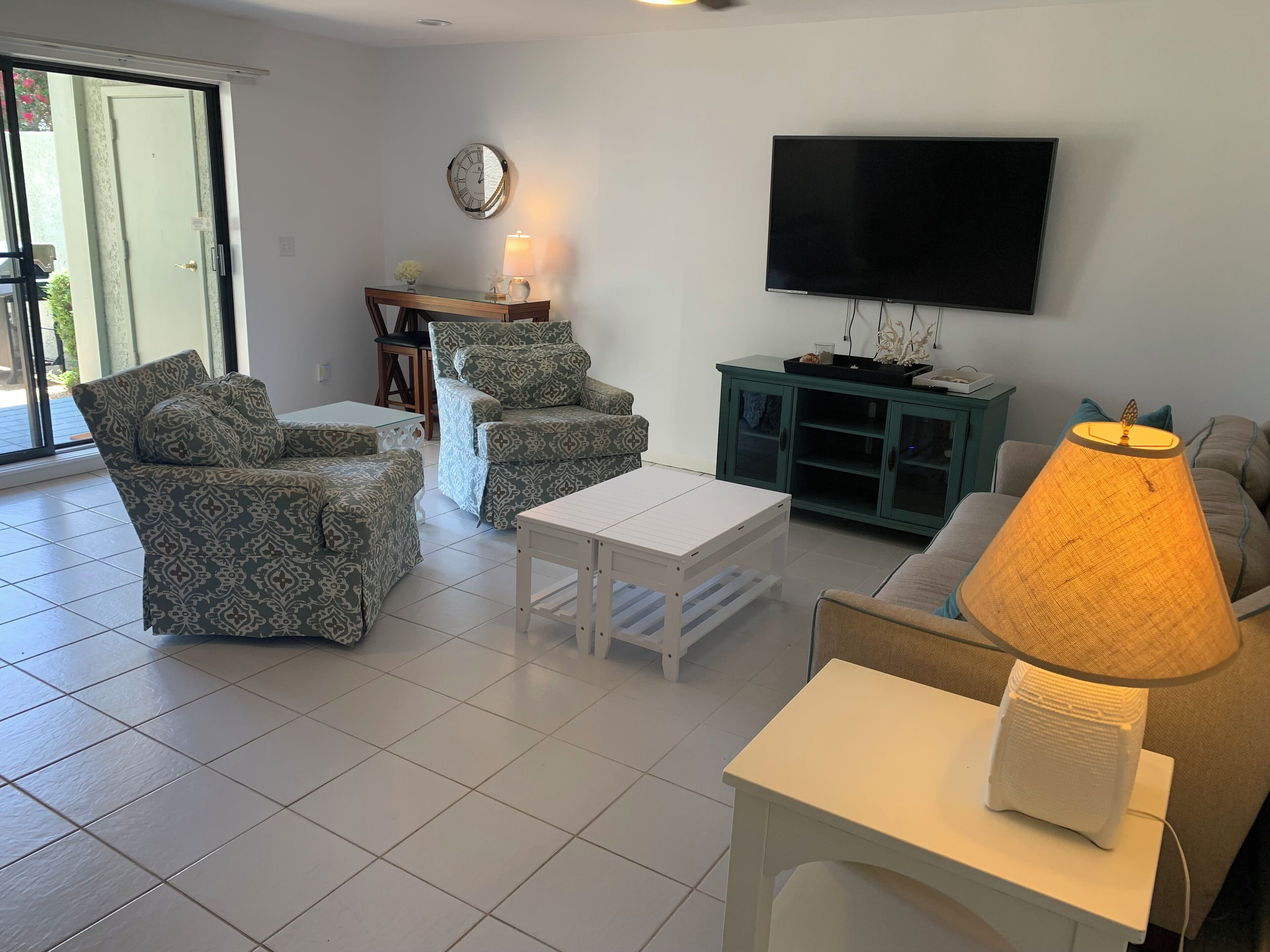 Una sala de estar con sofás estampados, una mesa de centro blanca, un televisor y una lámpara.