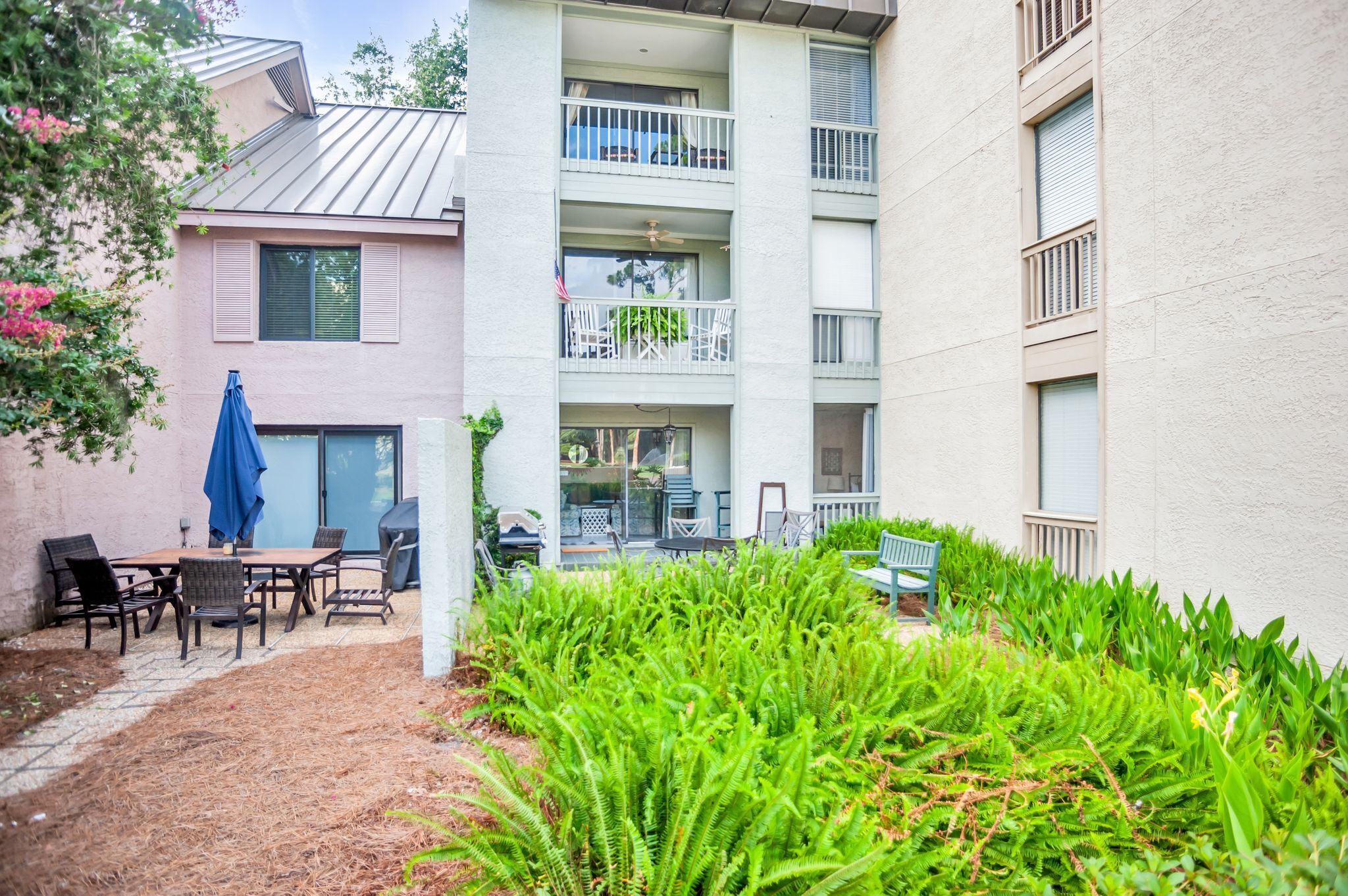 A multi-story building with a patio area featuring outdoor furniture and lush greenery.