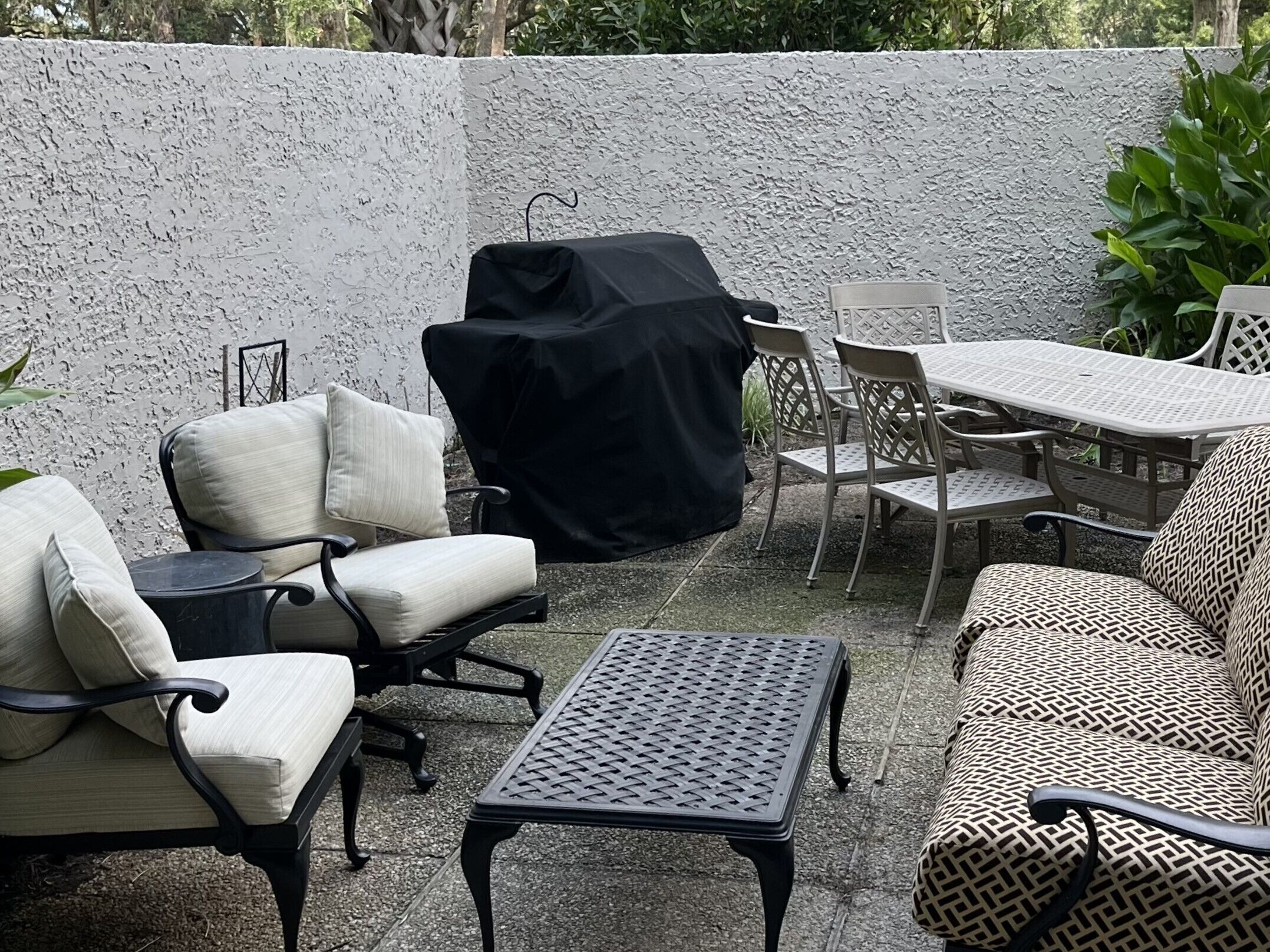 An outdoor patio area with a covered grill, cushioned chairs, a metal table, and a patterned sofa.