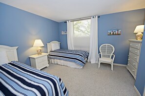 Ein Schlafzimmer mit zwei Betten, einem Sessel, einem Schminktisch und einem Fenster mit Vorhängen.