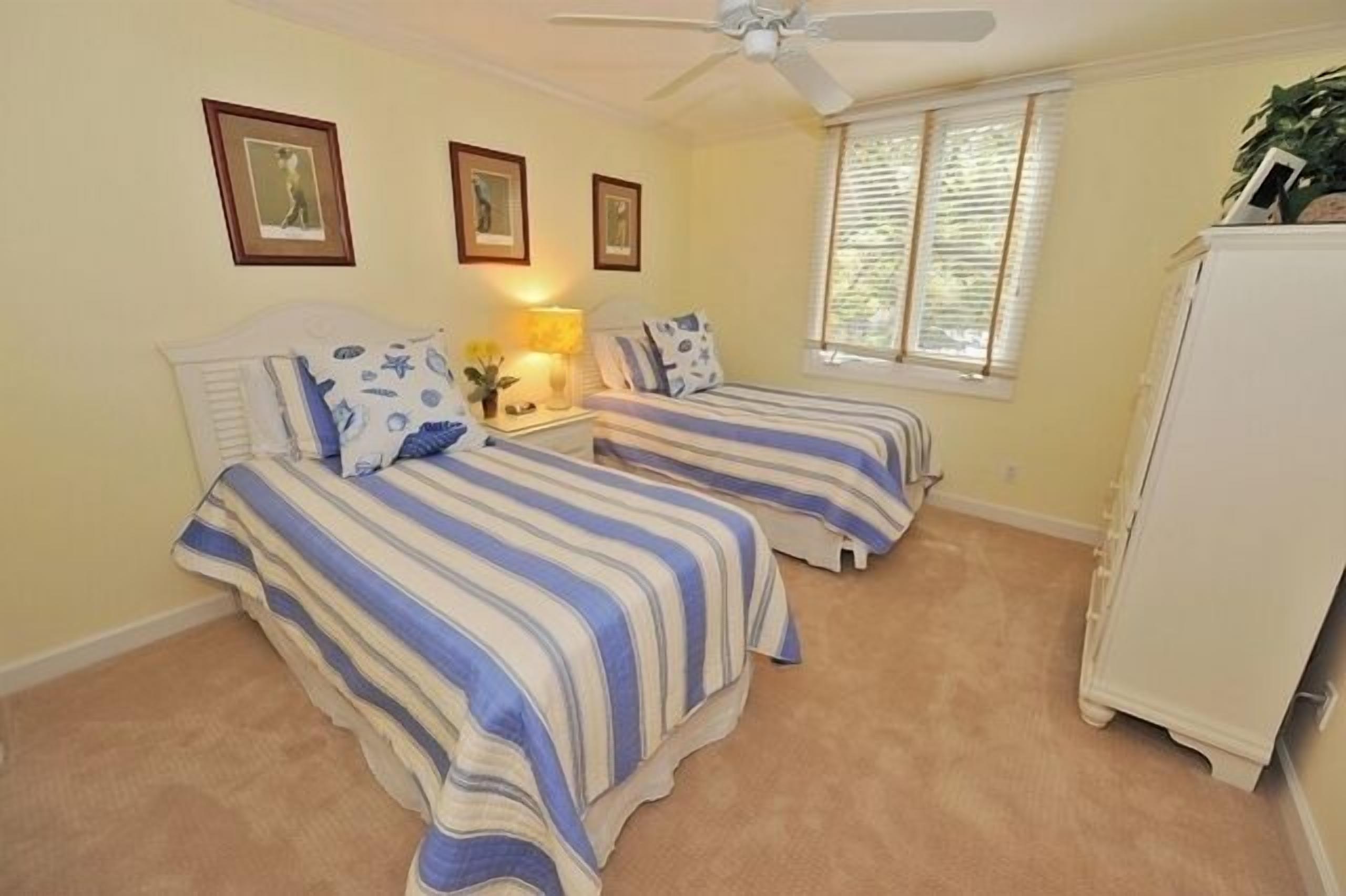 Quarto com duas camas, um ventilador de teto, uma janela com persianas e um armário branco.